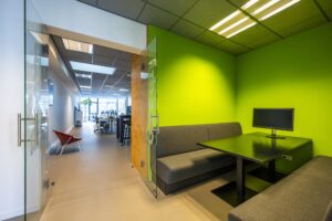 Moderne kantoorruimte aan de De Ruijterkade met vergaderruimte met felgroene muren, grijze banken en een computerscherm.